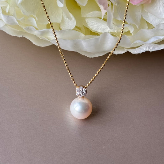 Pearl necklace with zirconias on a gray surface with white flowers in the background.