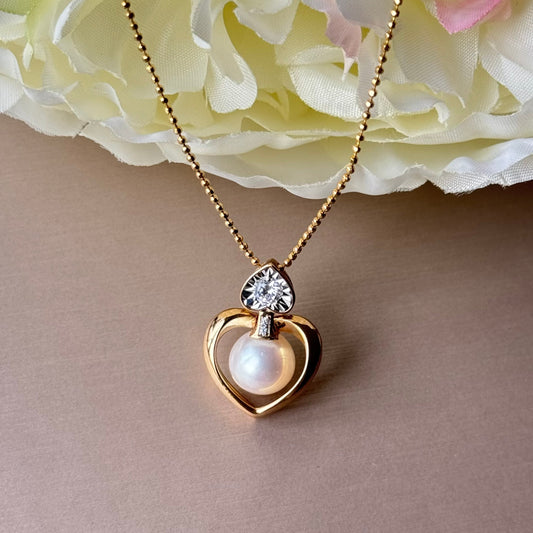 Gold necklace with a heart-shaped pendant featuring a pearl, against a soft pink floral background.