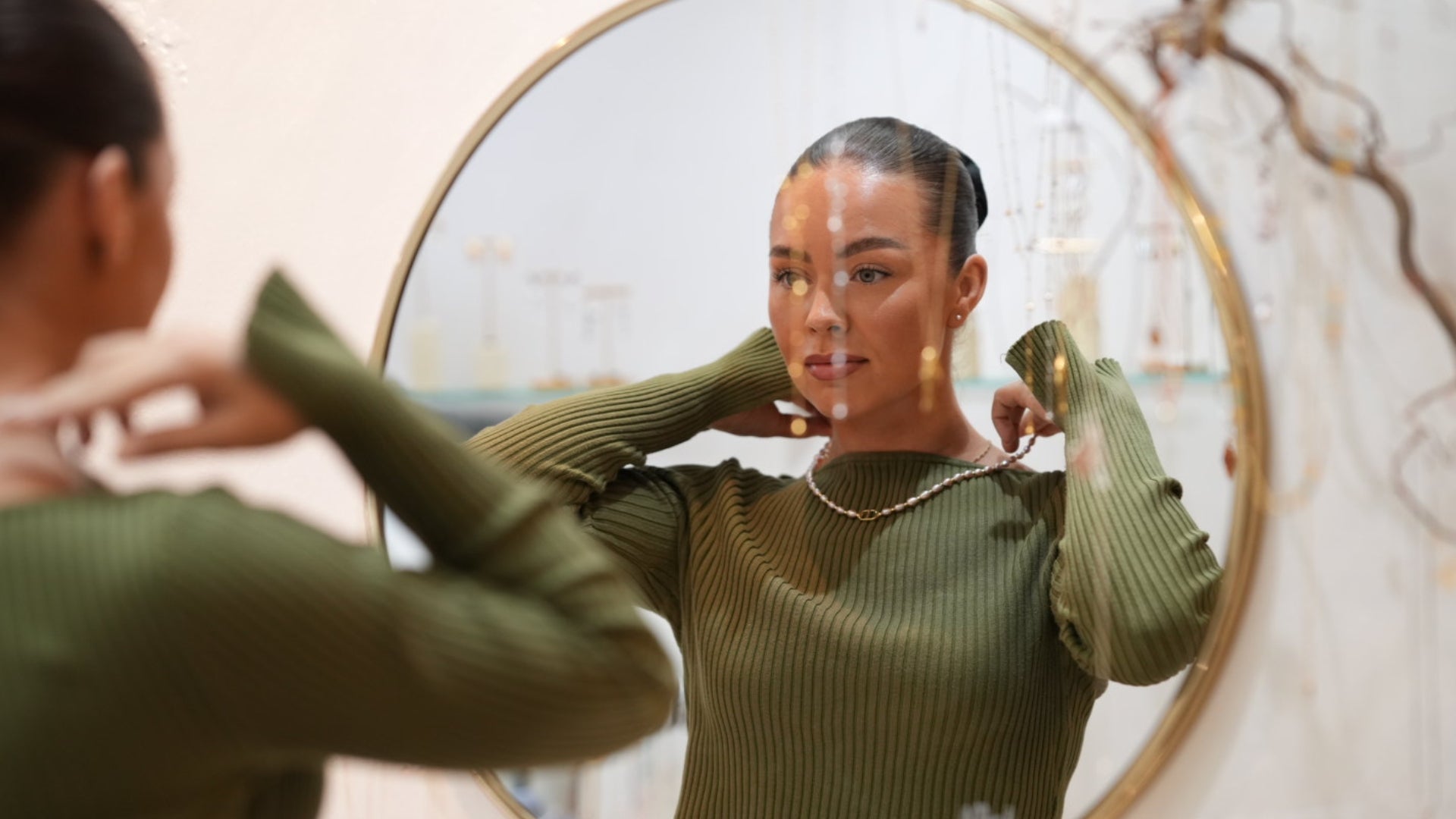 Woman adjusting her SKADIS pearl jewelry in front of a round mirror.