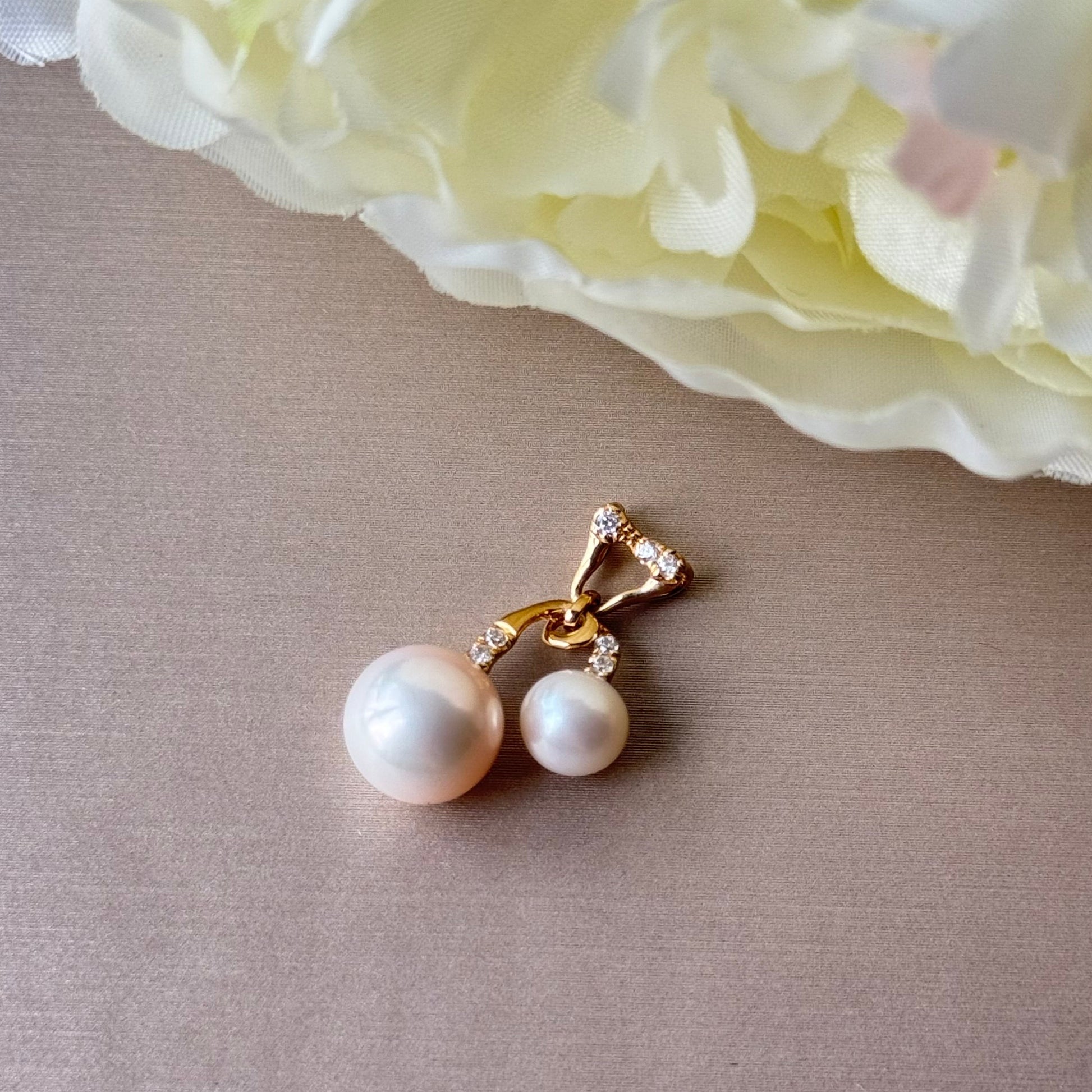 Pearl pendant with gold accents on a beige surface with a light pink flower in the background.