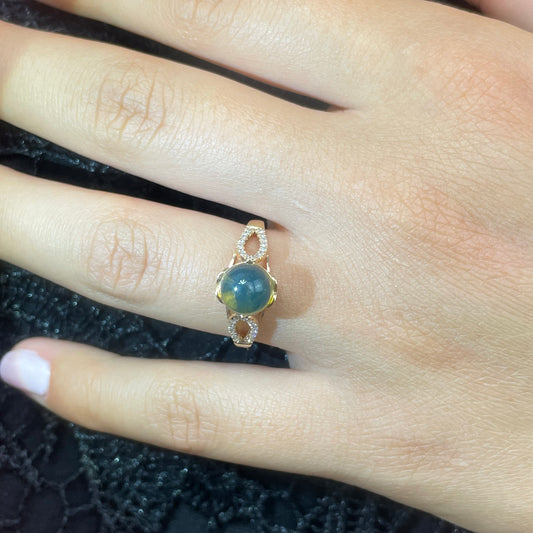 Gold ring with a blue amber and diamonds on a hand against a dark textured background