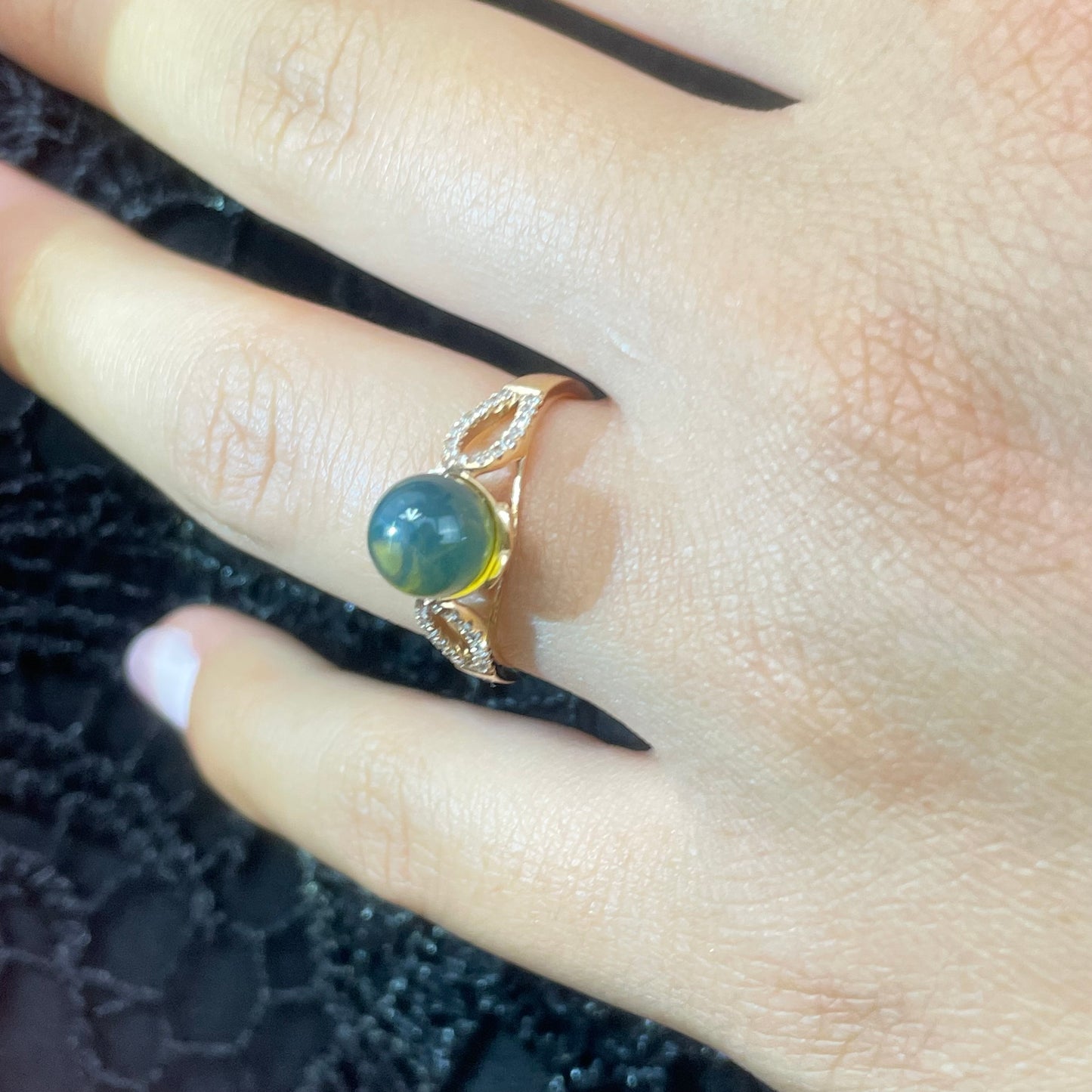 18k Gold ring with a blue amber and diamonds on a finger against a dark textured background