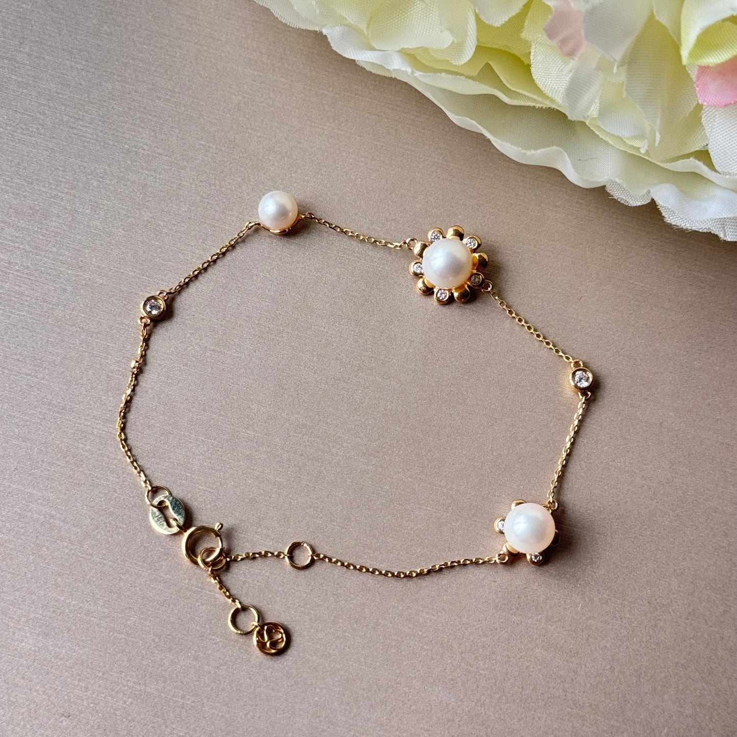 Gold bracelet with pearls on a beige surface with a flower in the background.