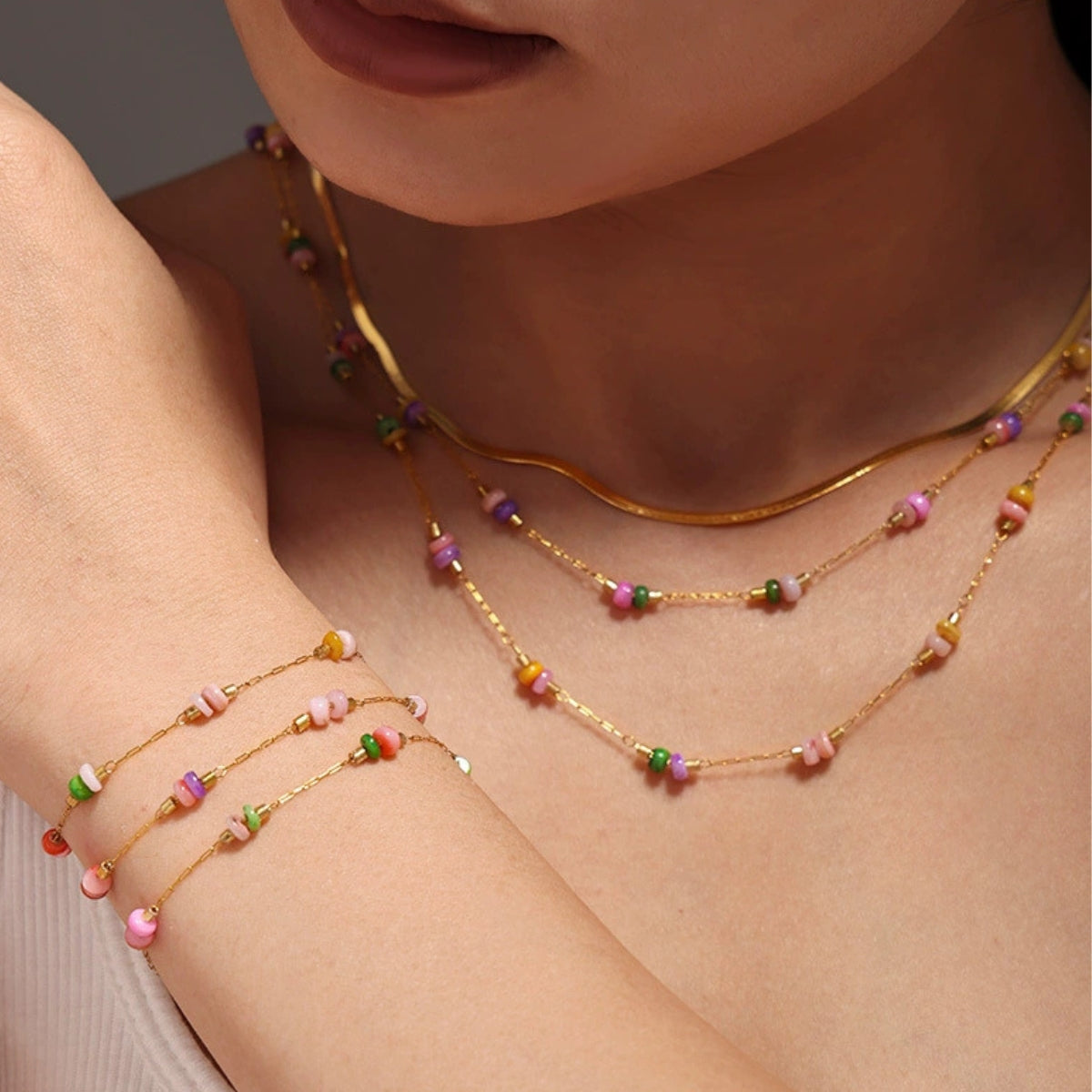 A person wearing multiple gold necklaces with colorful beads from SKADIS Jewelry