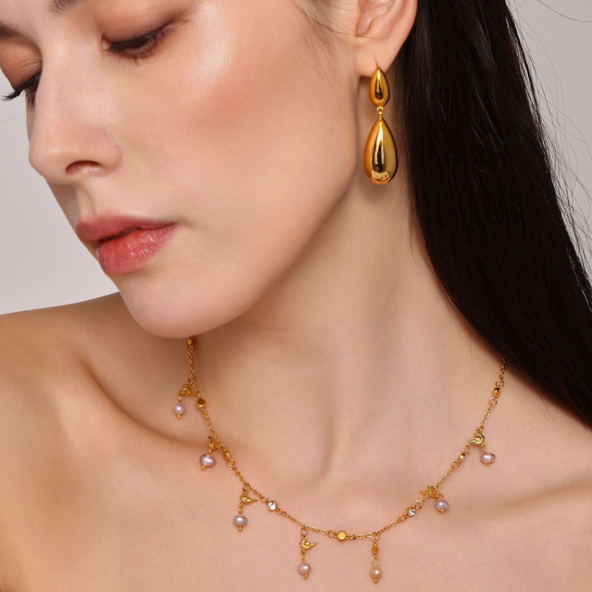  Woman wearing gold earrings and a matching necklace with pearls - SKADIS Jewelry