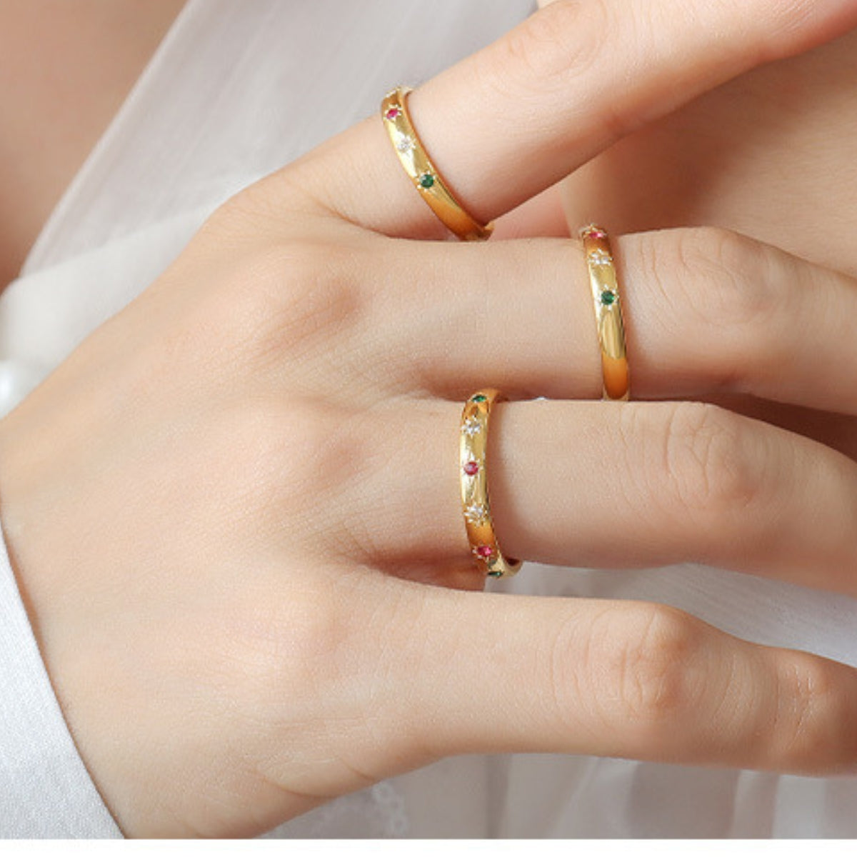Gold-plated rings with colorful zirconia on a person's fingers against a white background