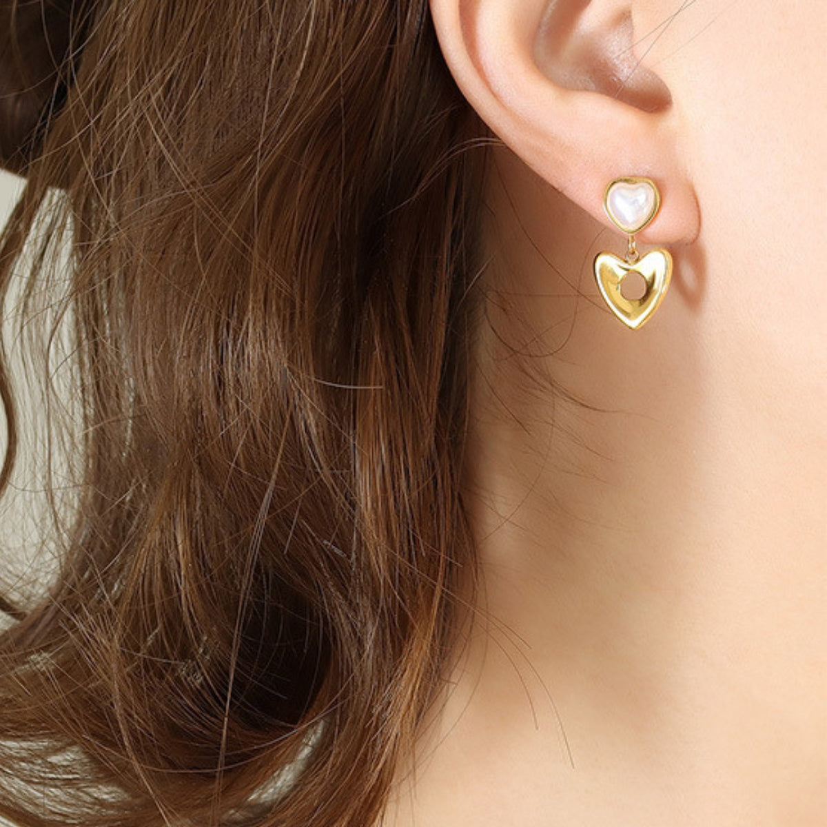 Gold heart-shaped earrings worn by a person -SKADIS Jewelry