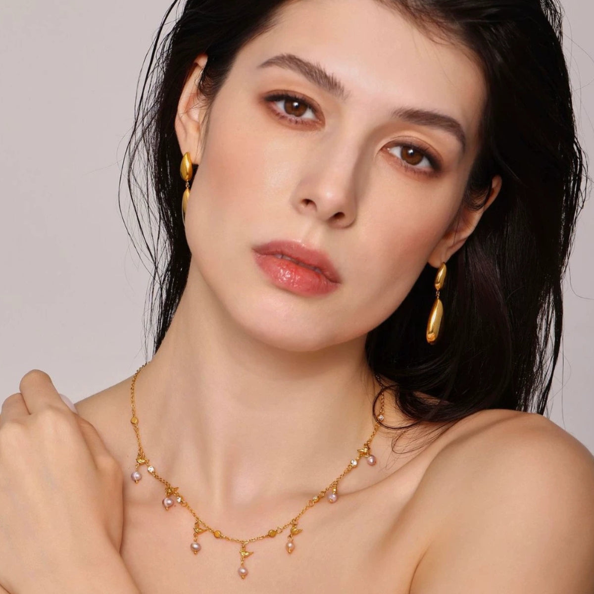 Woman wearing a gold necklace and earrings against a neutral background