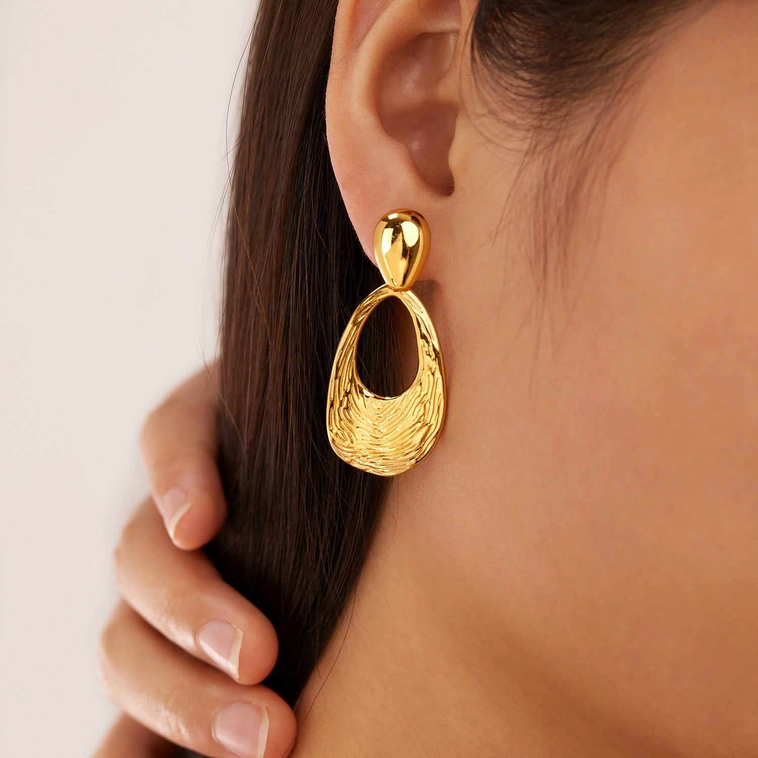 Gold earrings worn by a person from SKADIS Jewelry