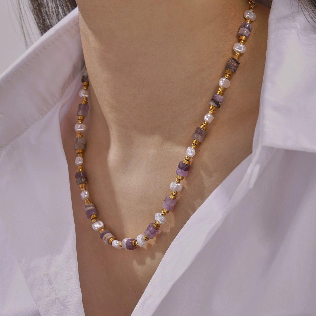 Necklace with purple and gold beads worn by a person in a white shirt.