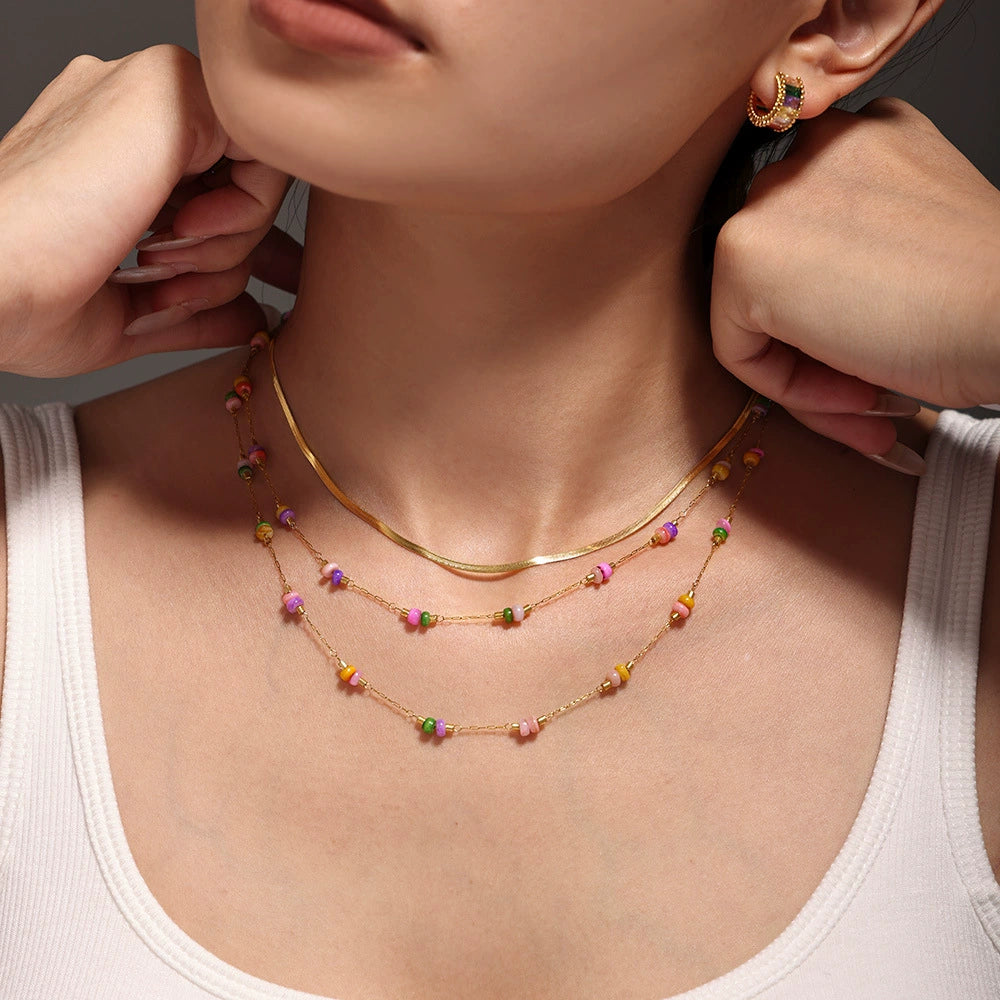 A woman wearing a gold necklace with colorful bead from SKADIS Jewelry